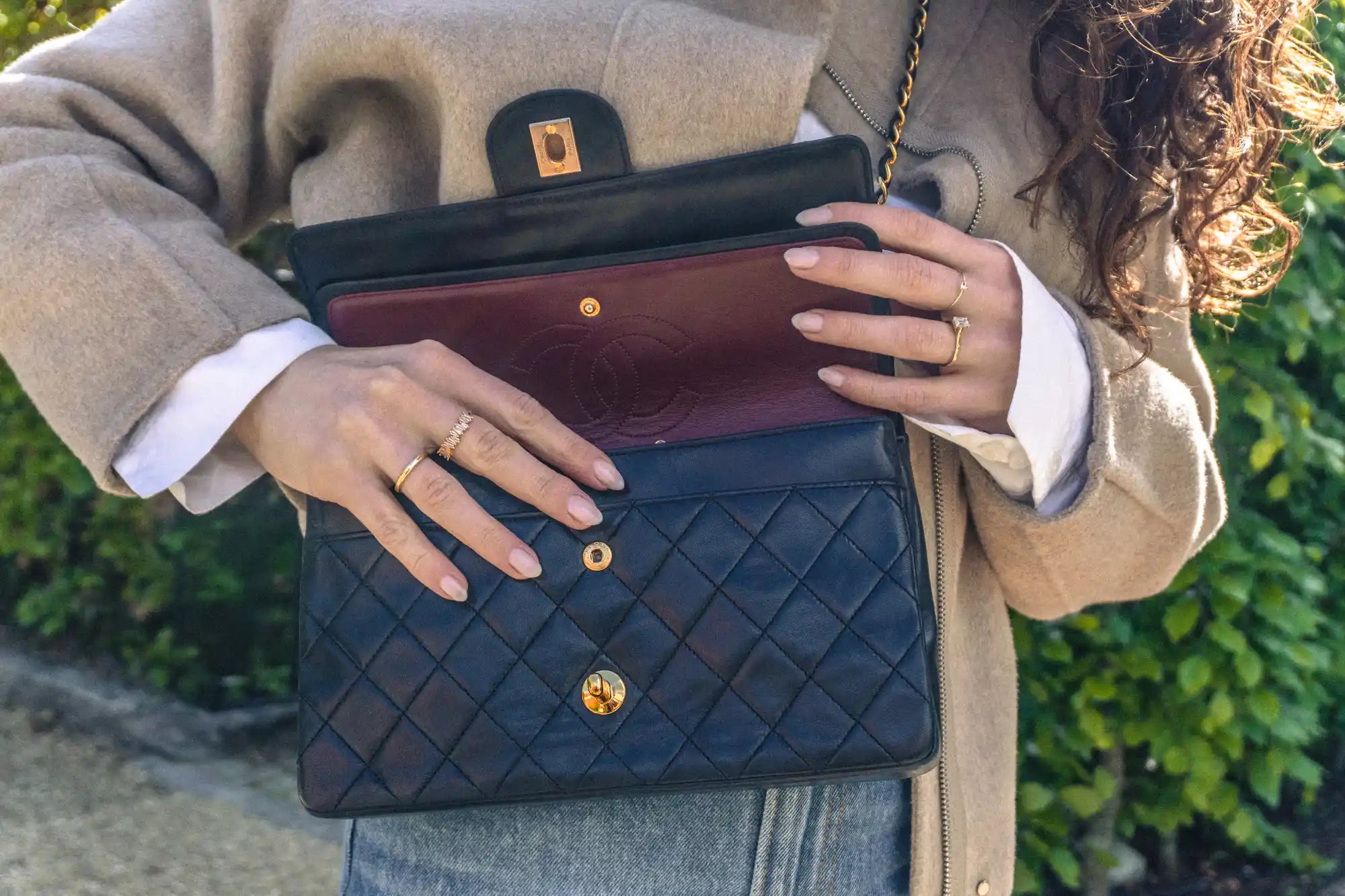 detail shot woman opening a black chanel medium classic flap showing burgundy inner flap
