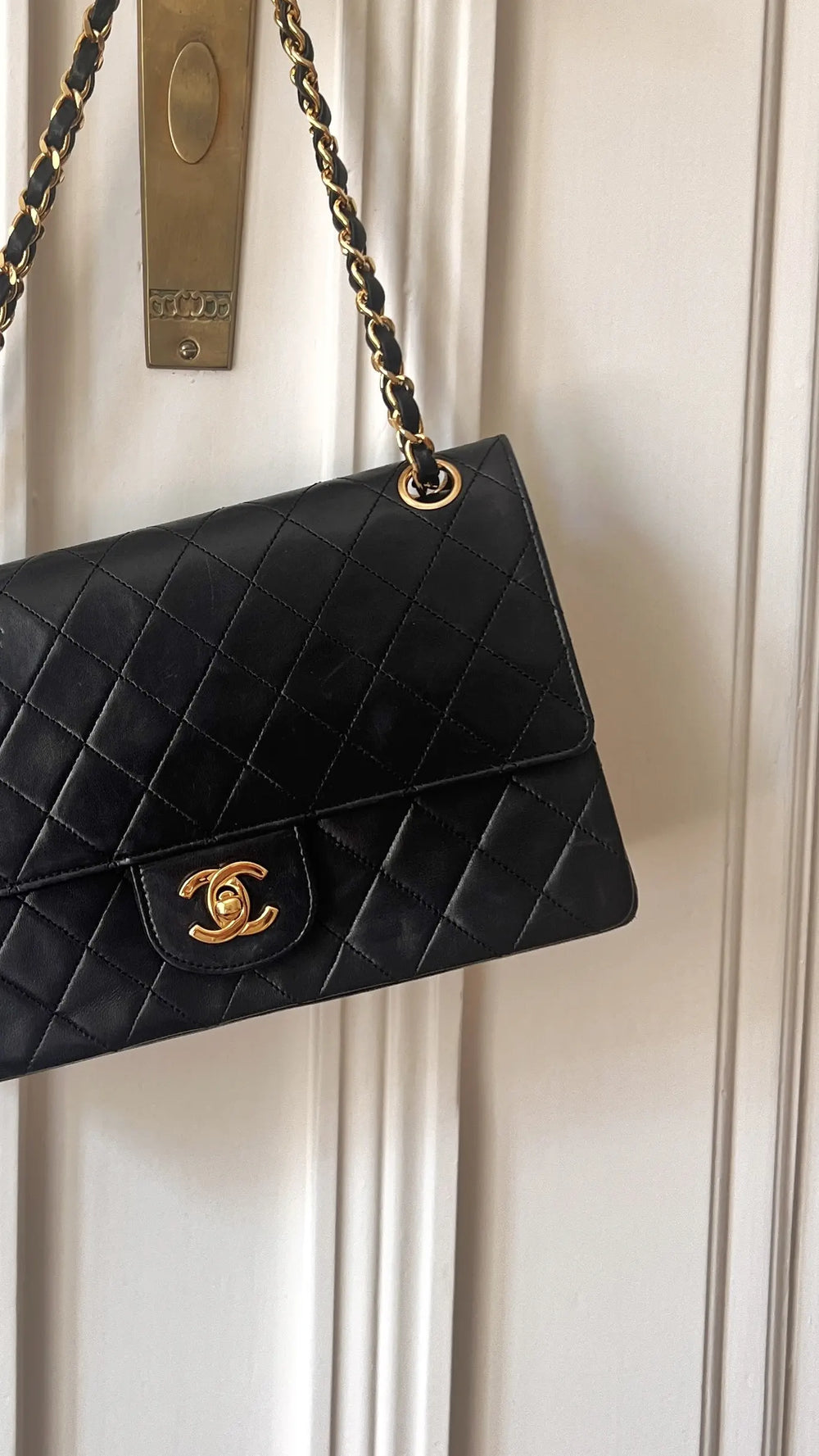a black chanel medium classic flap hanging on a door