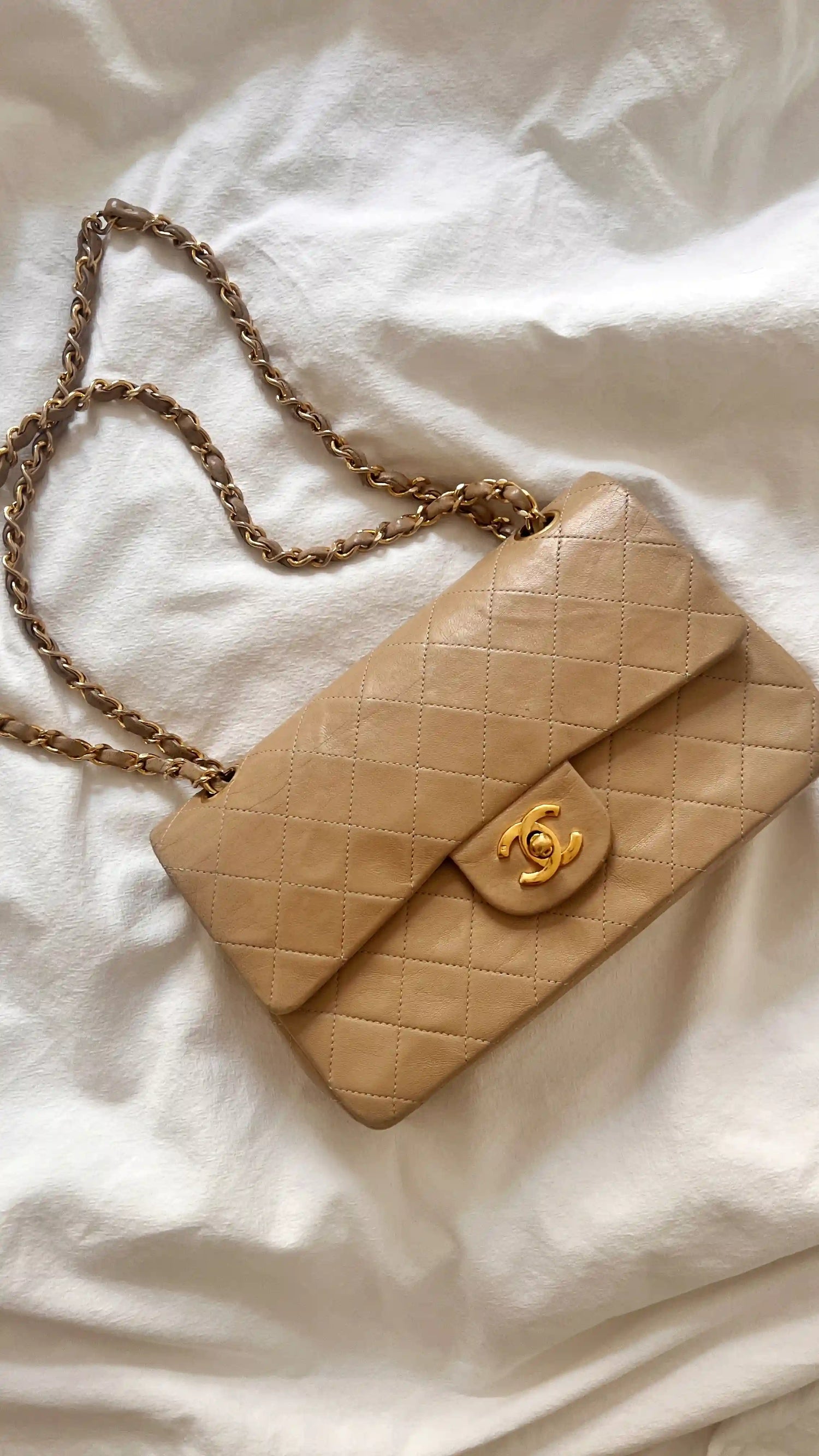 a beige chanel small classic flap lying on white sheets